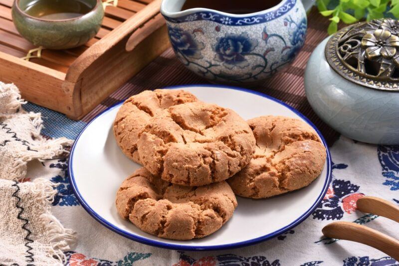 A white plate containing four Chinese walnut cookies, with various bowls and cups in the background