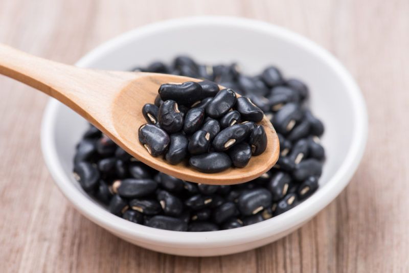 A white bowl containing black beans with a spoon