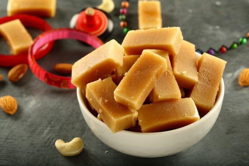 A white bowl with chunks of mysore pak cake, with cashwers and decorations on the table