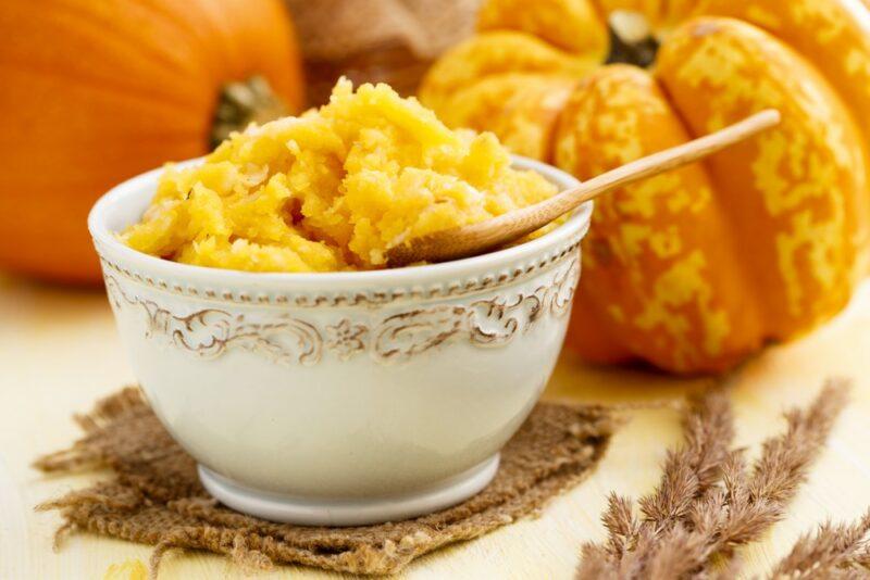 A white bowl filled with pumpkin puree in front of some pumpkins