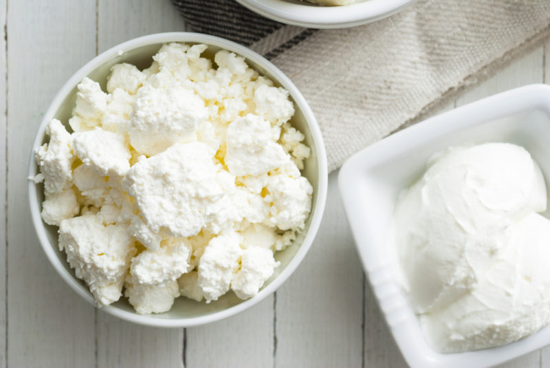 A white bowl filled with cottage cheese and a white square dish filled with cream cheese