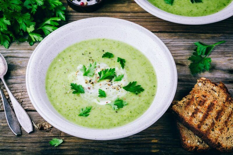 A white bowl filled with zucchini soup, with parsley pieces on the top