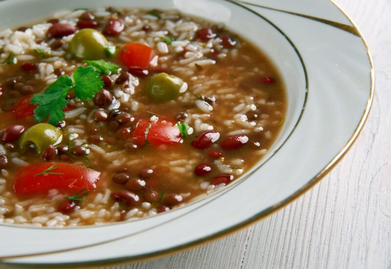 A white dish containing a stew called asopao de pollo that includes beans and olives