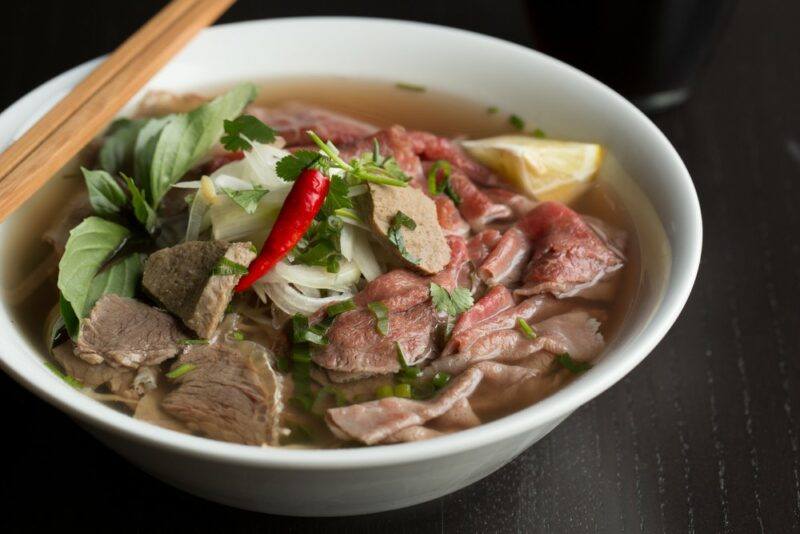 A white bowl containing beef pho, with two chopsticks laying over it