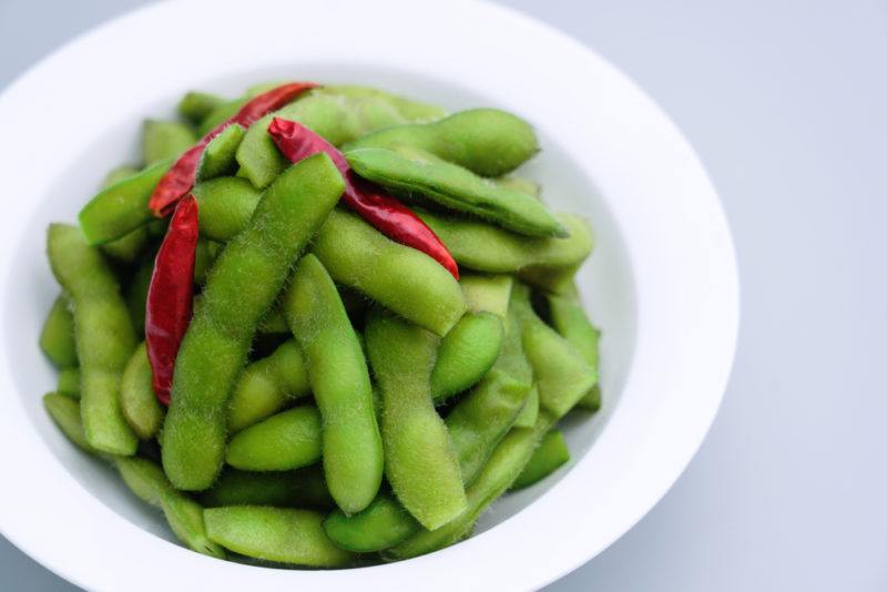 A white bowl with boiled soybeans and some chiles