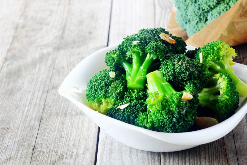 A white bowl with cooked broccoli and pine nuts