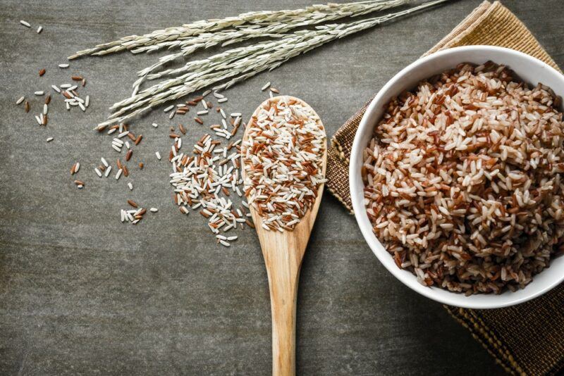 A bowl of brown rice on a cloth, next to a wooden spoon of the rice