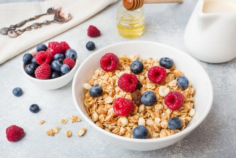 A white bowl with cereal and berries on a breakfast table, next to a small bowl of berries