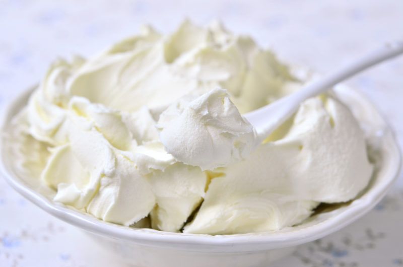 A white bowl of cream cheese with a spoon