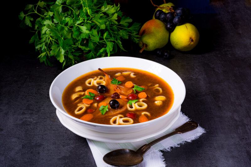 A white bowl containing a dish of czemina soup in front of greens