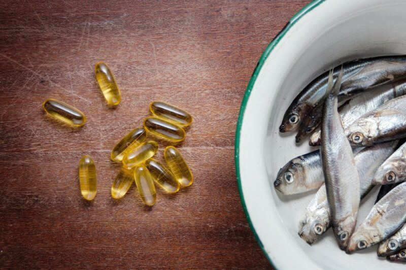 A wooden table with a bowl of fish, next to some scattered fish oil tablets