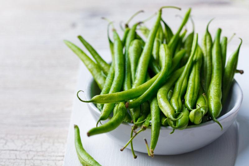 A white bowl filled with a large number of green beans