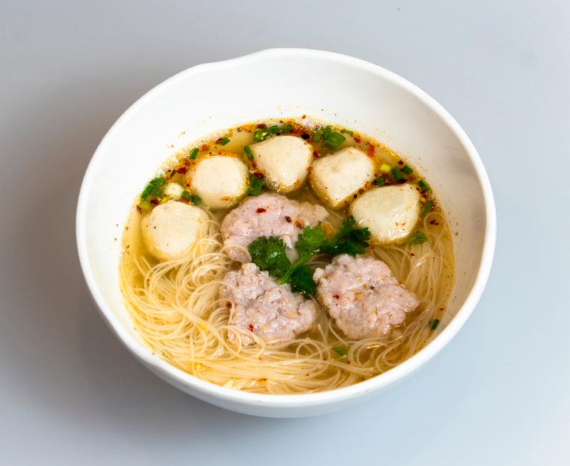 A white bowl of guay teow with noodles and dumplings