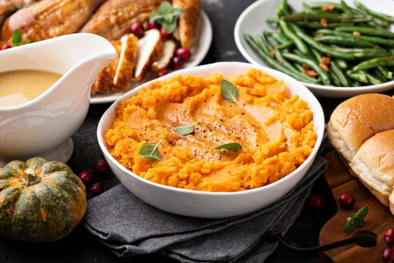 A white bowl with mashed sweet potatoes, in front of a white dish of beans, one of turkey, and a gravy boat