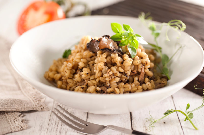 A white bowl that contains mushroom risotto next to a fork