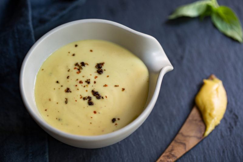 A small white bowl of a mustard-based dressing on a wooden board