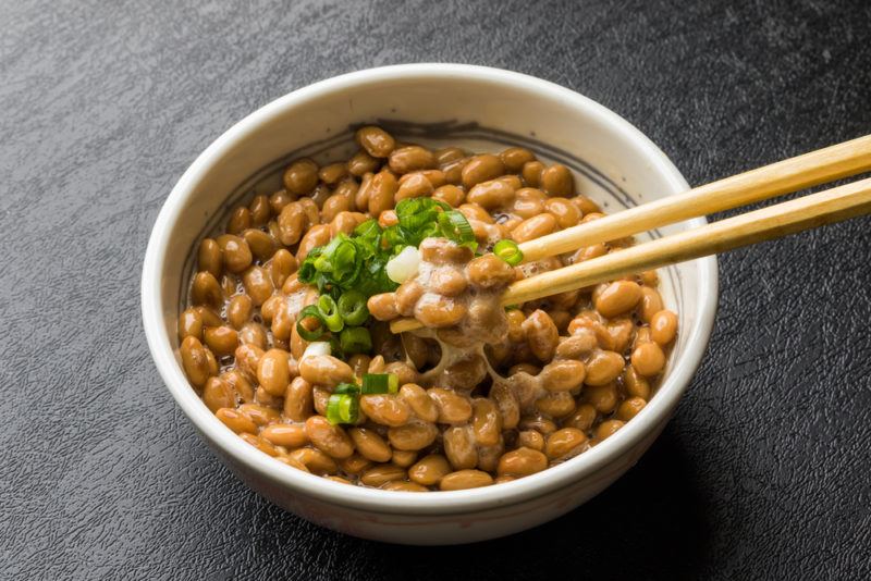 A white bowl containing natto, where some is being removed with chopsticks