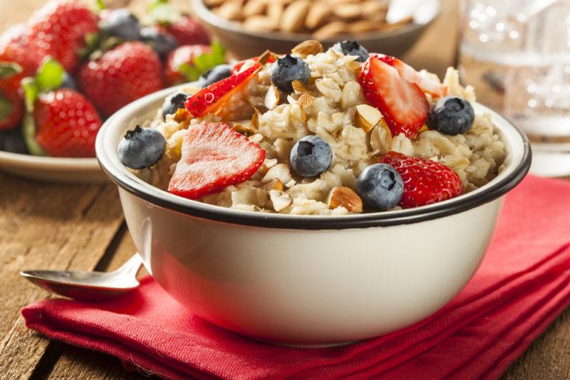 A white bowl that is filled to the brim with oatmeal, strawberries, and blueberries