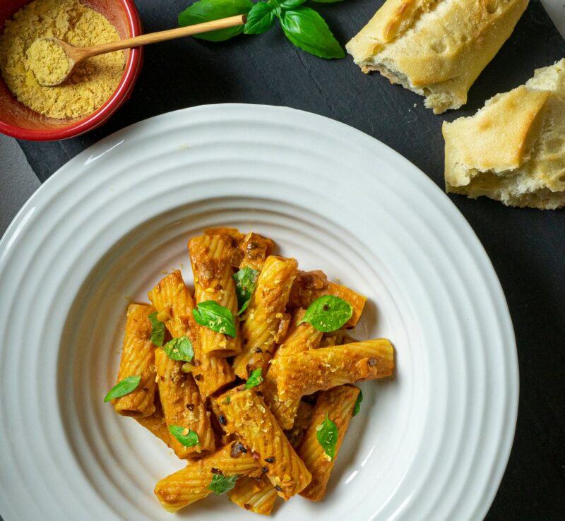 A shallow white bowl filled with pasta that has been seasoned with nutritional yeast