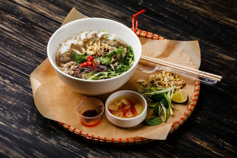 Someone's dinner that includes a large bowl of pho, a small bowl, and other ingredients