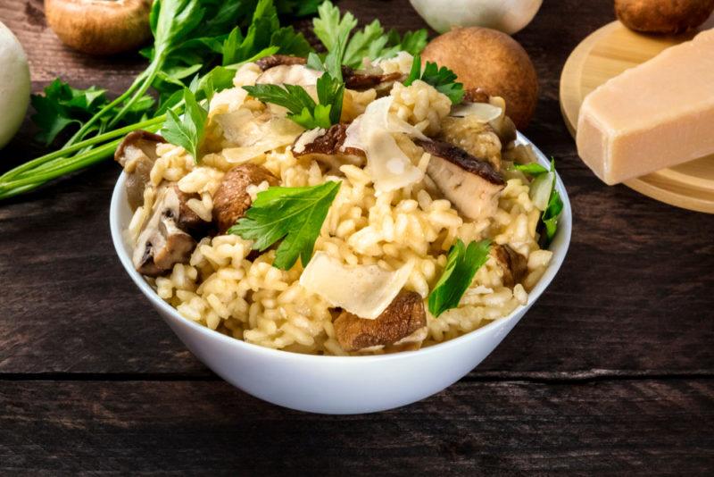 A white bowl of rice risotto with some greens on top, mushrooms, and parmesan cheese