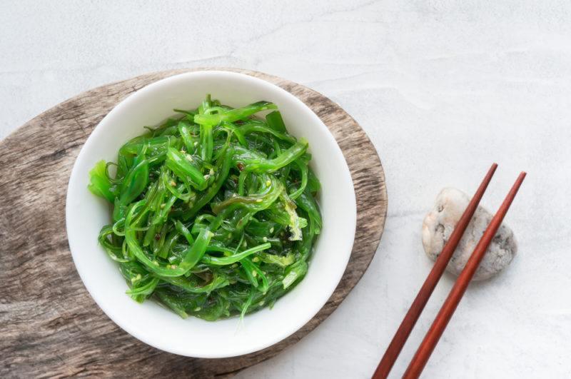 A white bowl with seaweed next to two chopsticks