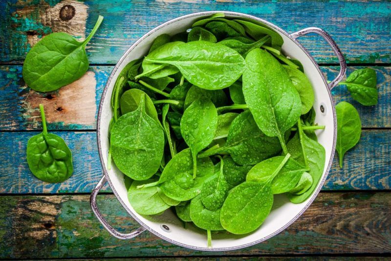 A white bowl with various raw spinach leaves