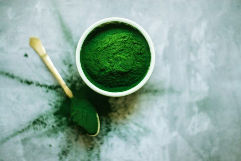 A small bowl with spirulina, next to a wooden spoon