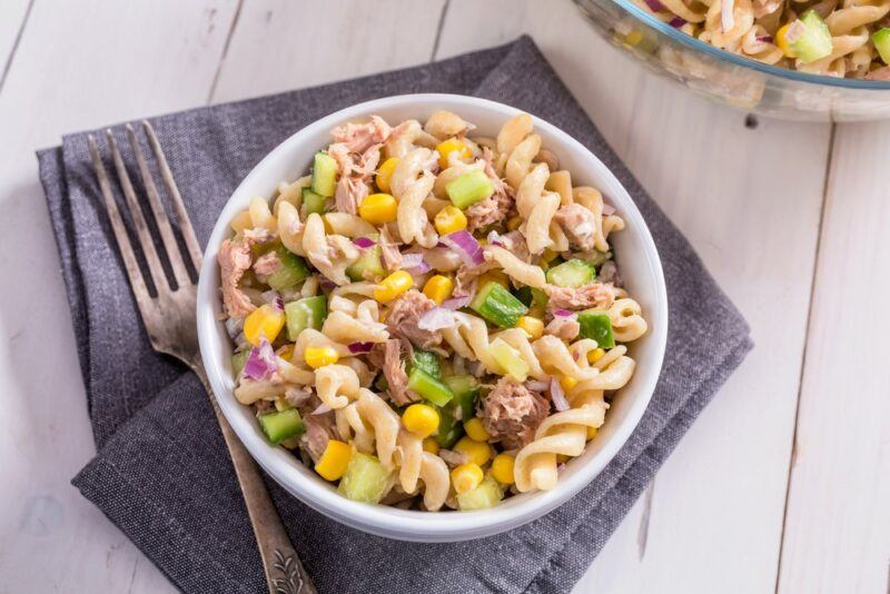 A white bowl containing a tuna pasta salad on a gray napkin next to a fork