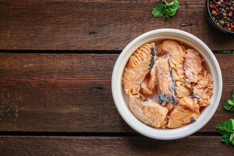 A small white bowl on a wooden table that contains canned salmon