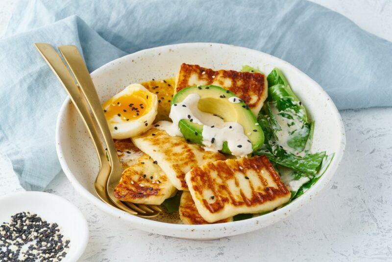 A white bowl containing halloumi cheese, eggs, and avocados