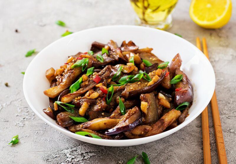 A large white bowl containing stir fried eggplant slices and vegetables