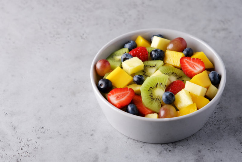 A white bowl on a marble table that contains fruit salad