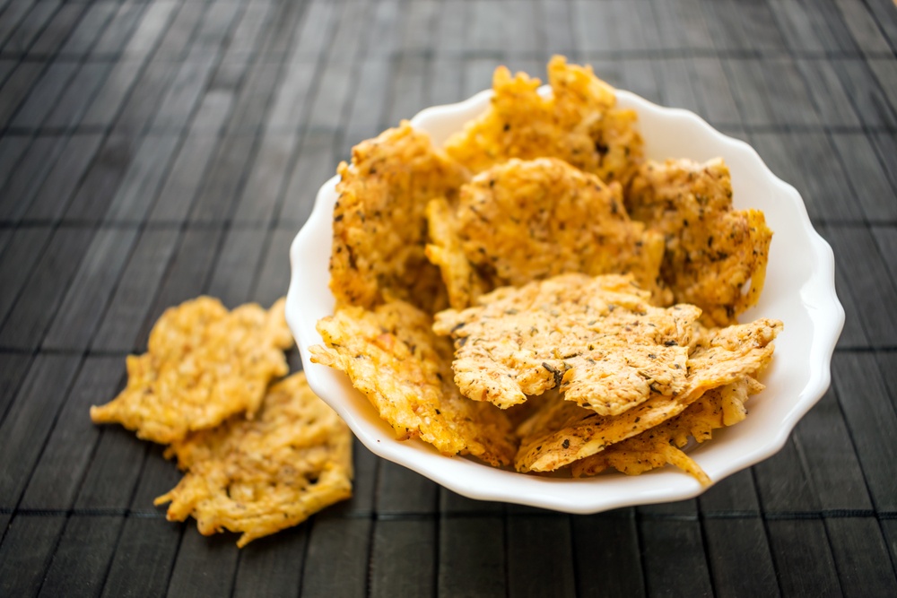 A white bowl of cheese crackers and a few on the table