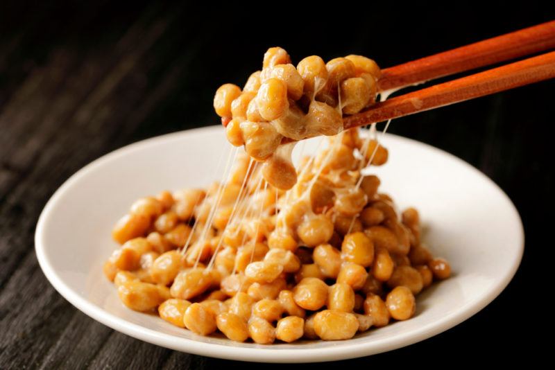 A white bowl of natto that is being pulled out with chopsticks