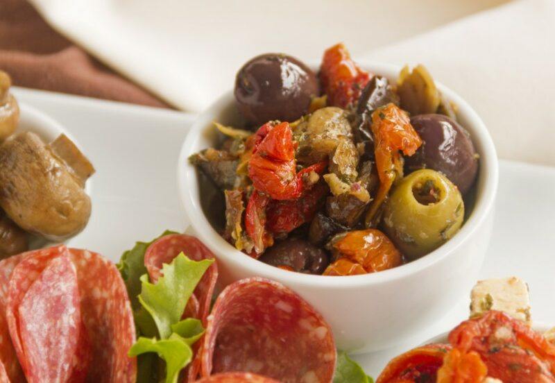 A white dish containing lettuce and salami, plus a small white bowl of olives and sundried tomatoes