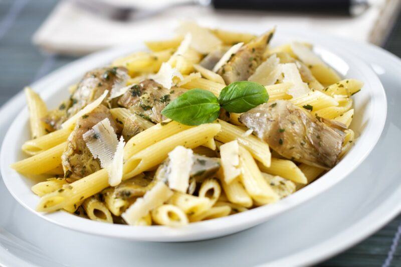 A white bowl with pasta, artichokes and cheese