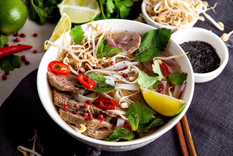 A white dish that contains a fresh meal of Vietnamese pho