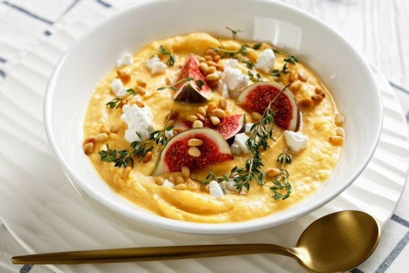 A large white bowl containing polenta or something similar, with figs, pine nuts, and other ingredients as a garnish