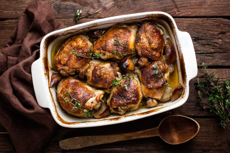 A white casserole dish that contains cooked chicken thighs