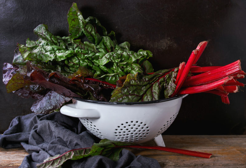 A white colander filled with dark leafy greens, including Swiss chard