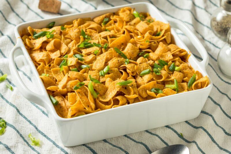 A white square dish containing a Fritos pie on a striped