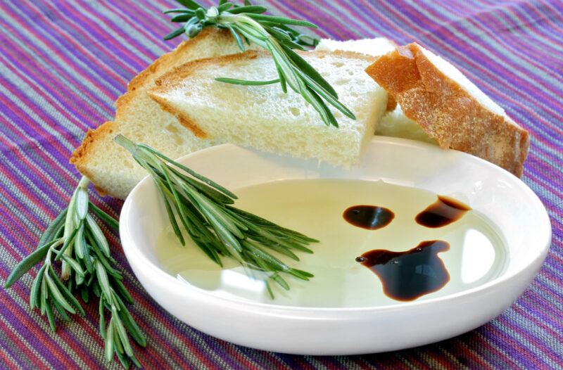 A white dish containing olive oil and balsamic vinegar, with some bread in the background