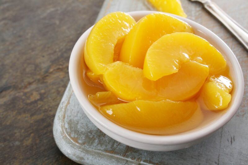 A white bowl containing sliced peaches from a tin on some type of tray