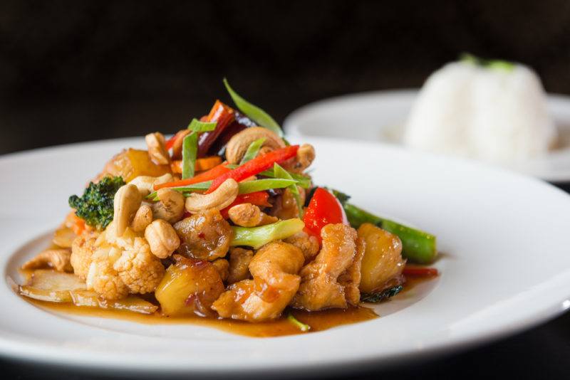 A white plate with a chicken cashew meal and rice in the background