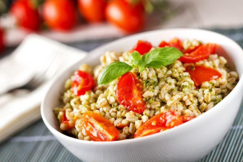 A white bowl containing cooked barley with pesto, and tomatoes