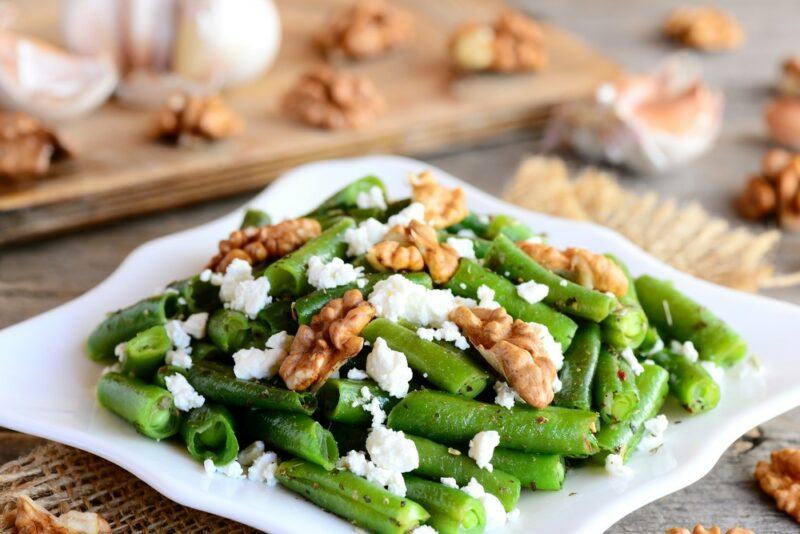 A white plate with fresh green beans, goat cheese. and walnuts