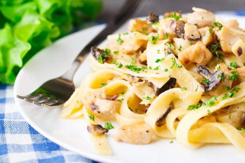 A white plate of creamy chicken pasta and a fork