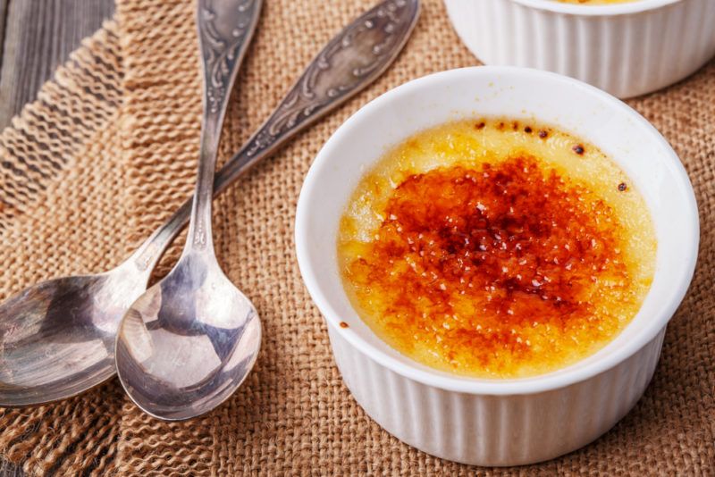 Two white dishes of creme brulee with two spoons