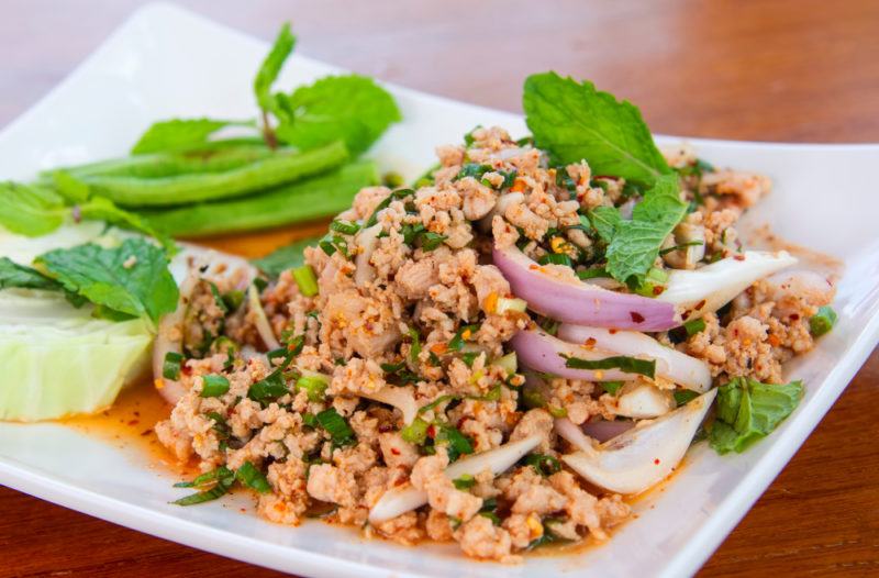 A white plate with laab fried meat and some greens